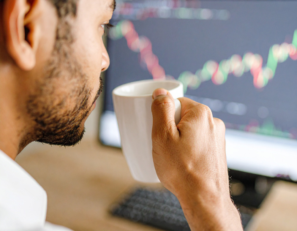 Man sipping on mushroom coffee while looking at computer screen with stock charts.